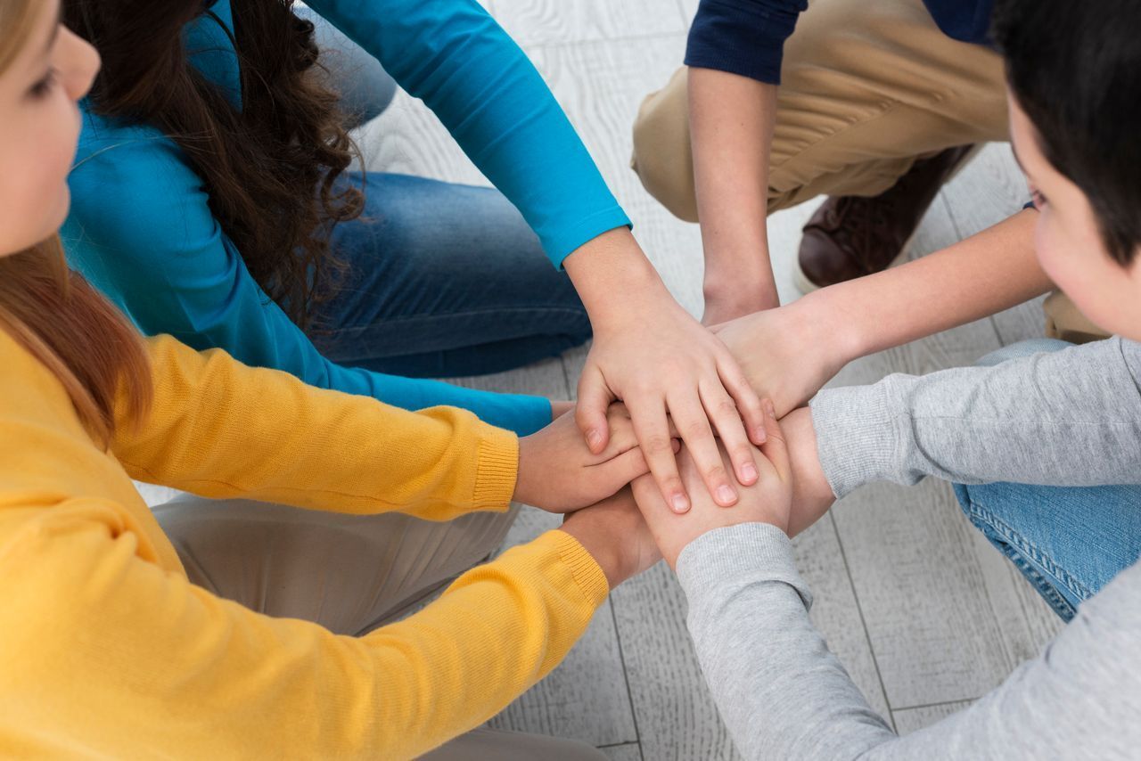 La imagen muestra a un grupo de niños poniendo sus manos juntas en un círculo